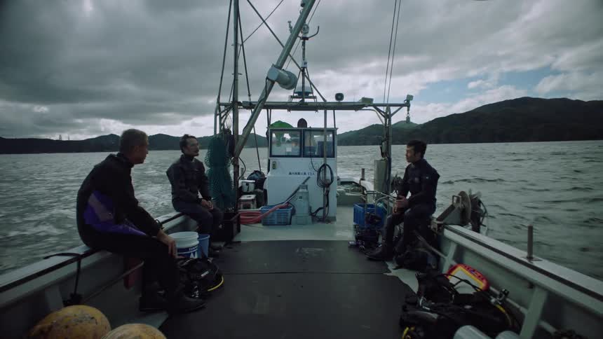Group of men wearing wet suits sitting on a boat sailing on a lake