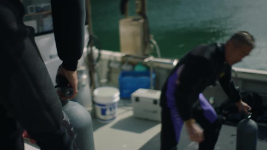 Two men are putting air tanks into a boat docked along the coast