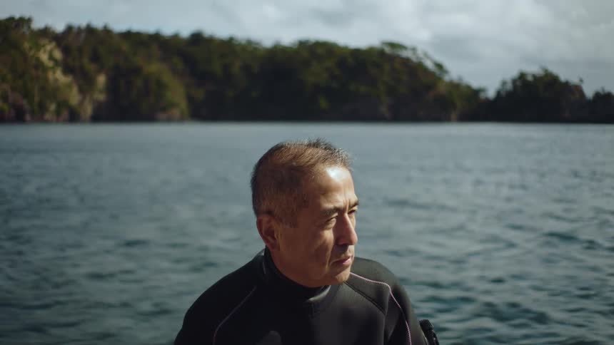 Mature man wearing a black wetsuit sitting on a boat sailing on a lake