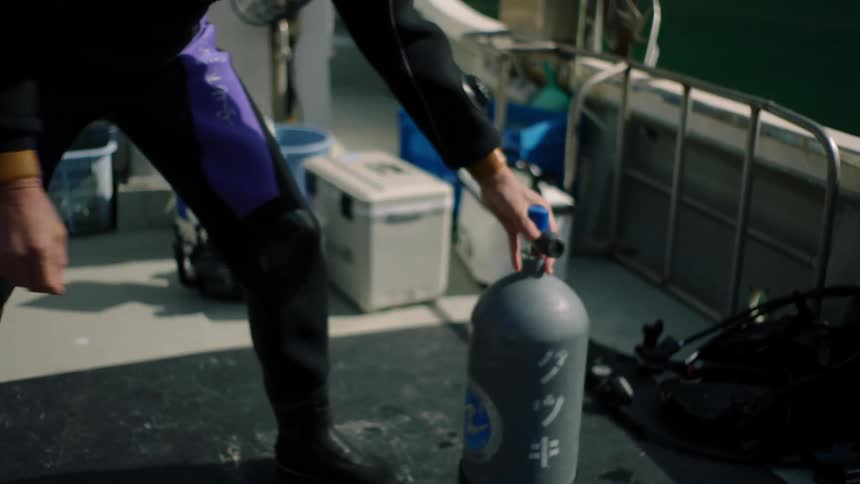A man stretching and then grabbing an oxygen tank from another man near him and setting it in a boat