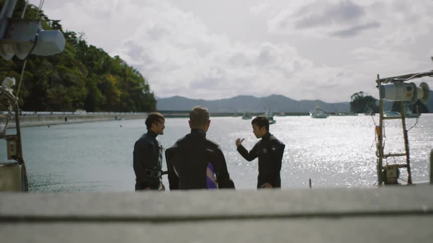 Three men are getting swimming gear on near a body of water