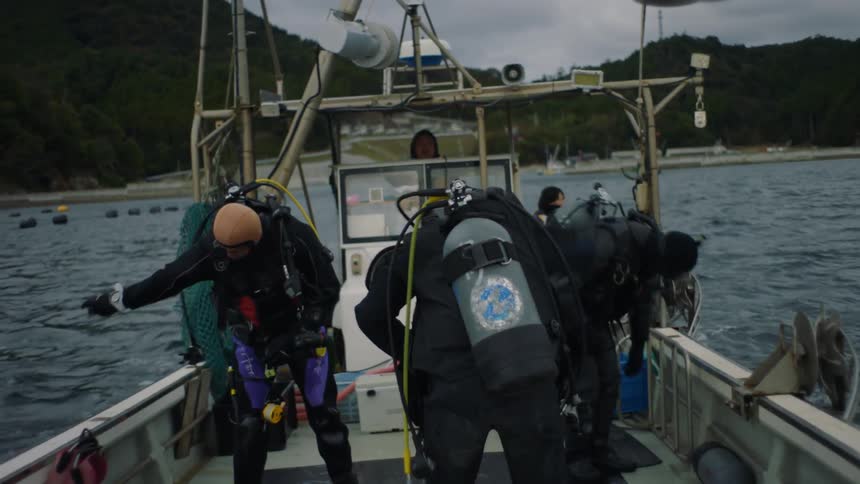 A group of men get their scuba diving equipment ready as they stand on a boat that is bobbing up and down on the water