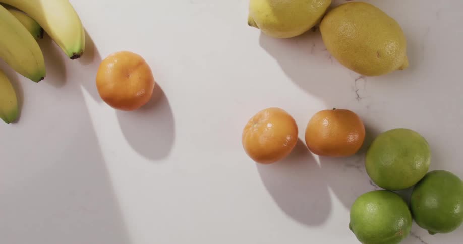 Top down view of mandarins falling over a white table with other fruits