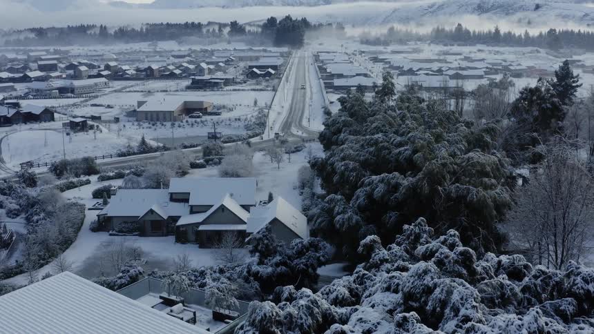 Vehicles drive along highway through snow covered town surrounded by mountains