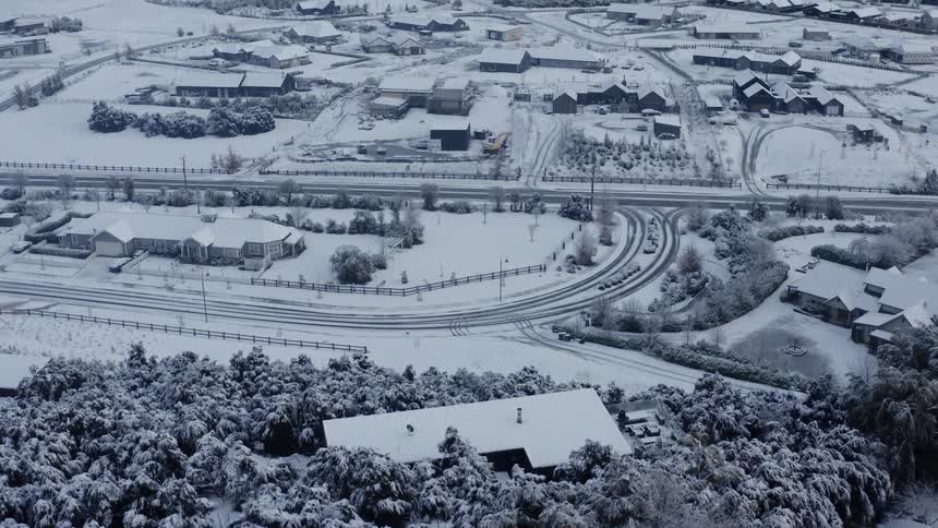 An aerial of a snow covered village with mountains in the distance through the fog