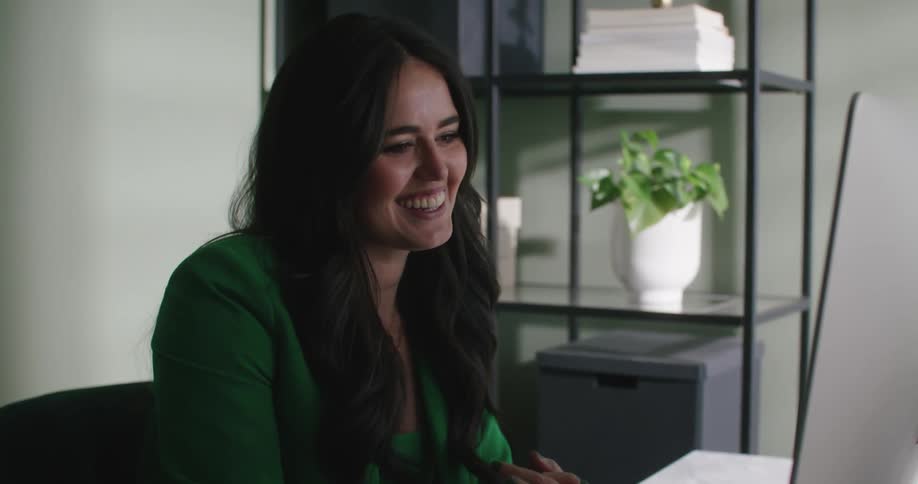 Woman smiles and gestures while sitting in office during a video call