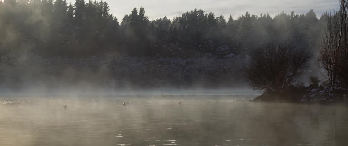 A lake with morning fog rolling off it surrounded by forests