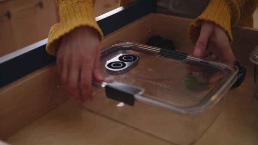 A girl wearing a yellow sweater opens a drawer and takes a plastic container
