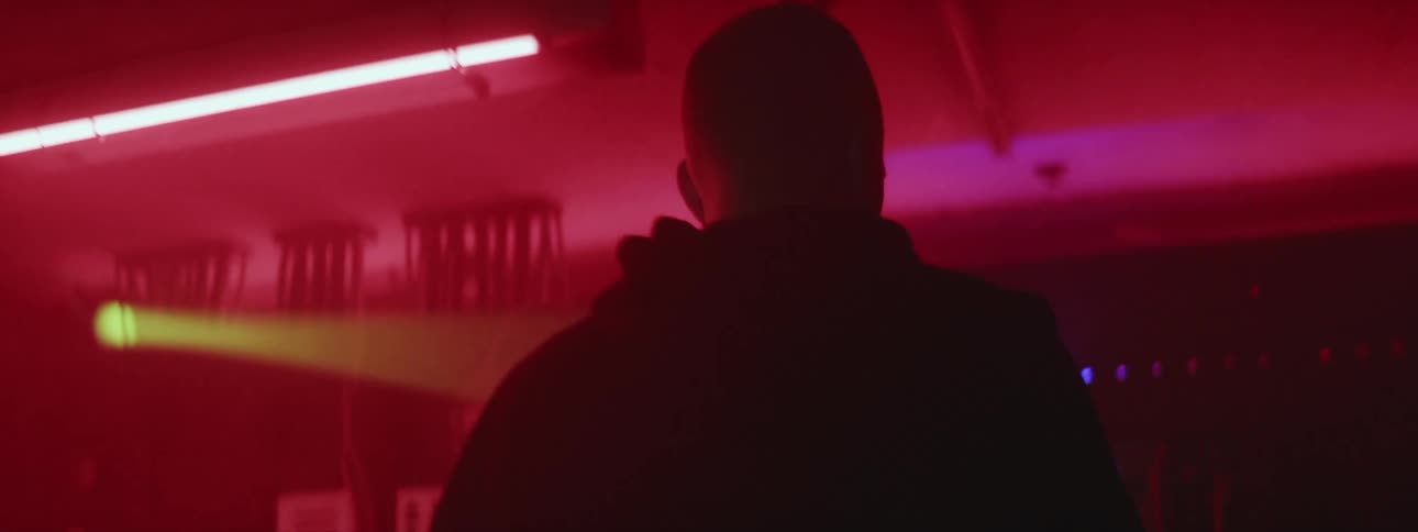 A silhouette of a man standing in a dark room lit by neon lights as he stands in front of a server board