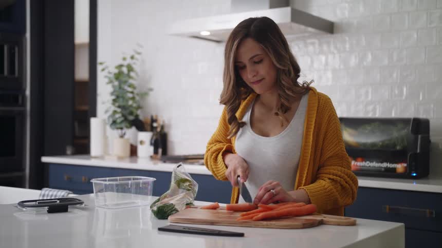 A woman chops whole carrots in her kitchen