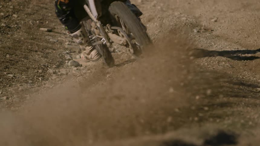 Rocks and dirt fly into the air as a motorcycle slides across the ground