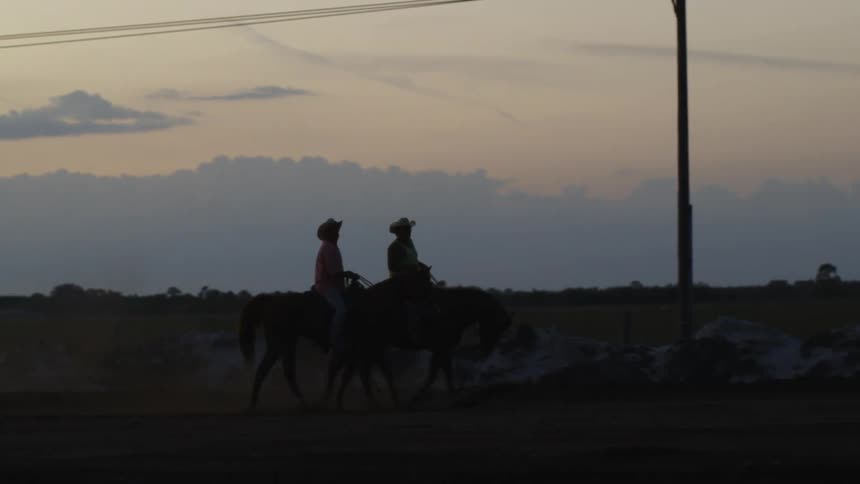 Two people ride horses at sunset