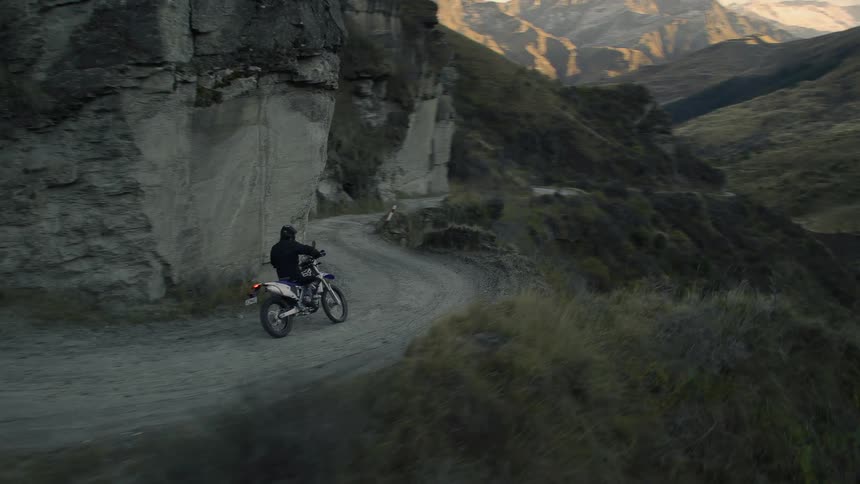 Motorcyclist rides along road hugging steep mountain side over drop