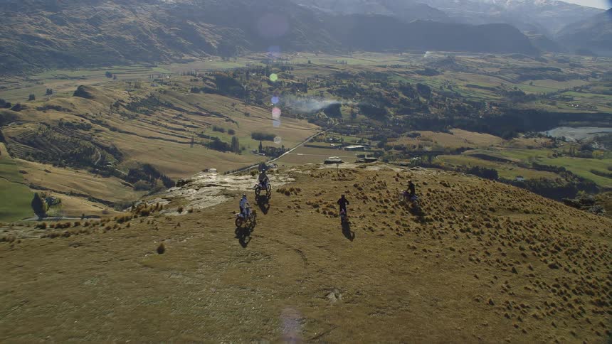 Four motorcycles stop at the edge of a cliff overlooking a rural area with mountains in the distance