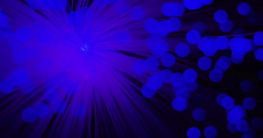 Strands of light change from blue to purple as blue orbs glow and move in the darkness