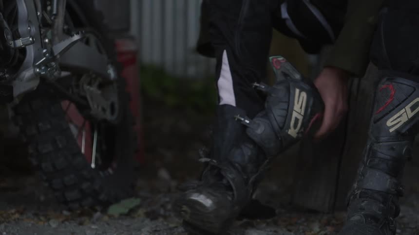 A man is sitting near a motorcycle putting boots on his feet