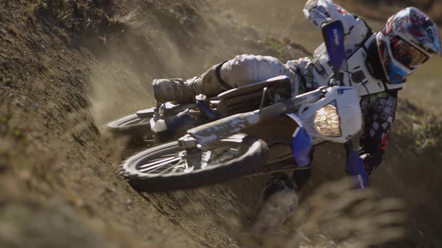 A person riding a dirt bike with a helmet and protective gear on on a dirt track going around a corner