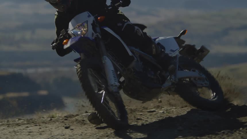 Rocks and dirt fly into the air as a motorcycle slides across the ground as they travel on mountain terrain