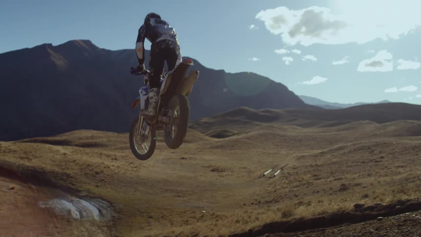 A motorcycle traveling in the mountains leaps in to the air as it flies down a hill