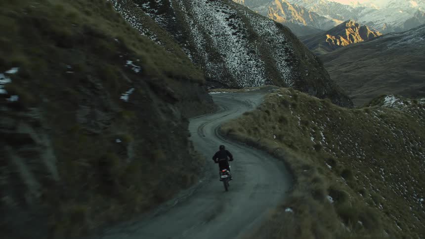 A person rides a motorcycle along a winding mountain road during the day