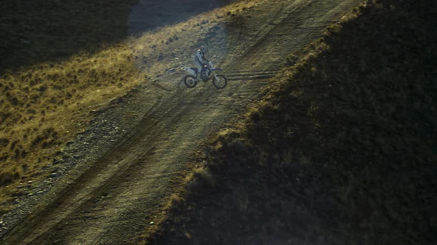 A motorcycle traveling on mountain terrain leaps across the road and moves down a steep hill