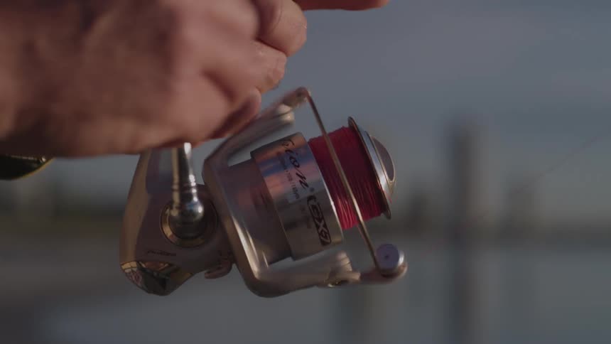 A person reels in their fishing line while using a fishing rod while outdoors