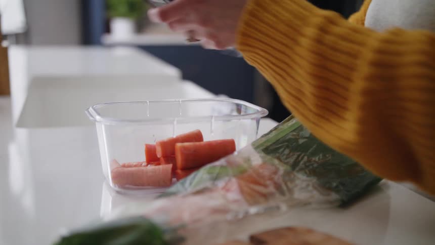 A girl picks up cut carrots from a cutting board and puts them into a plastic container