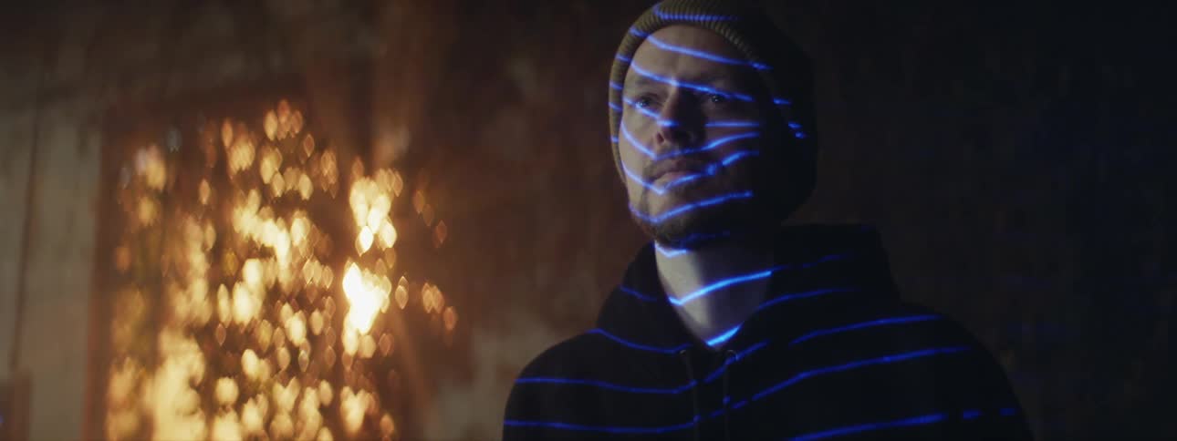 Close up of the head of a man with bright electric blue lights projected on his face