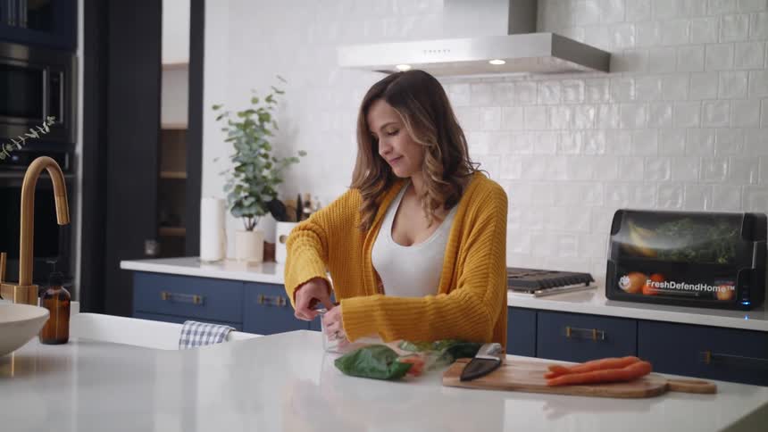 Woman opens food storage container in kitchen standing next to vegetables on a chopping board