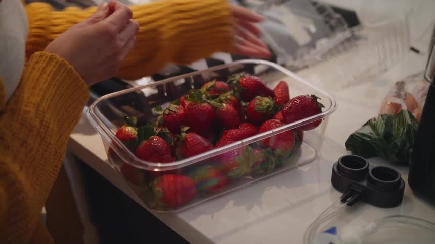 A person pouring strawberries into a container and putting the top on the container