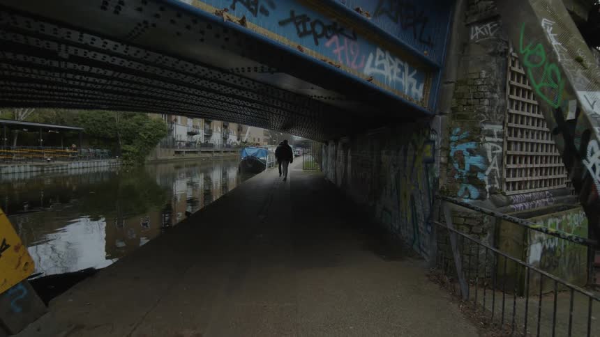 Pedestrians walk under graffiti covered bridge over river