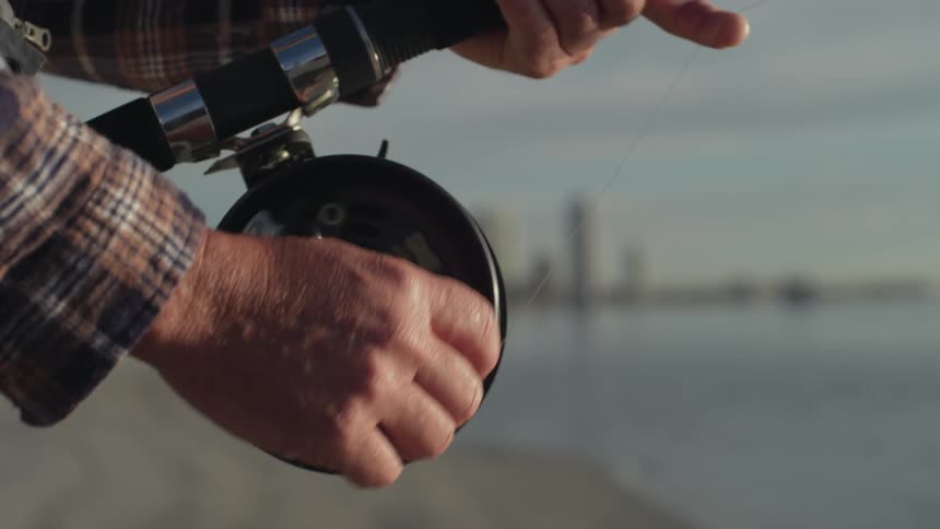 A man fishing reels in his fishing rod