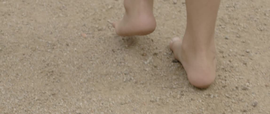 A person walks barefoot on pebbly ground