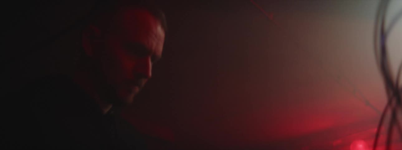 Man manipulates connecting wires on large panel in foggy room with flashing light in the background