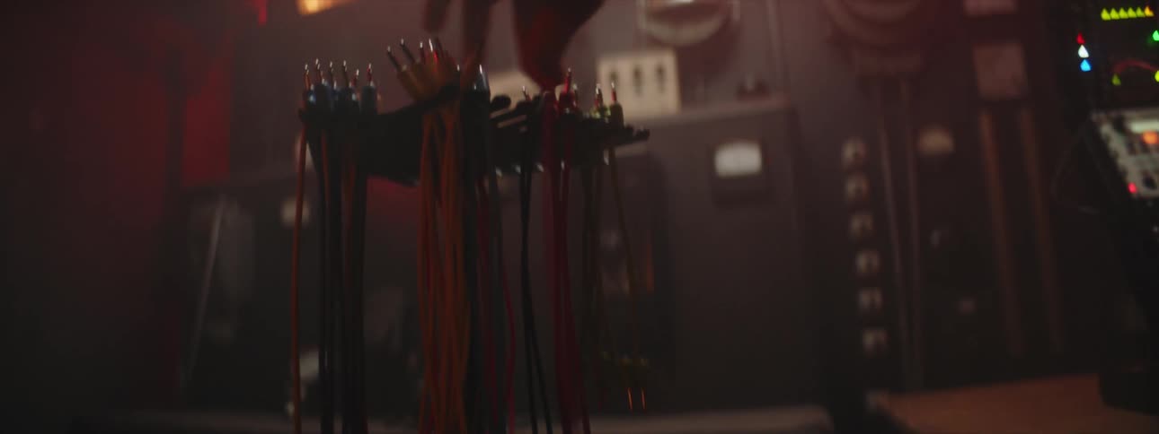 A man reaches over and takes a wire from a rack of wires near a computerized machine with many glowing lights