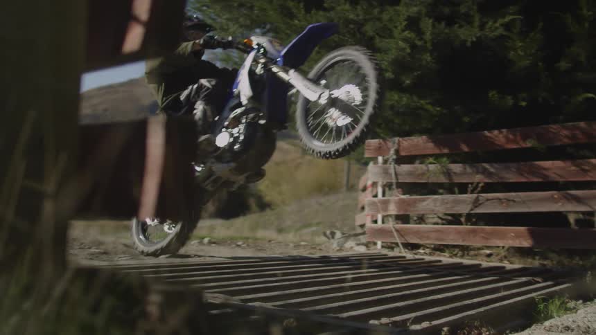 A person riding a dirt bike doing a wheelie over a wooden bridge