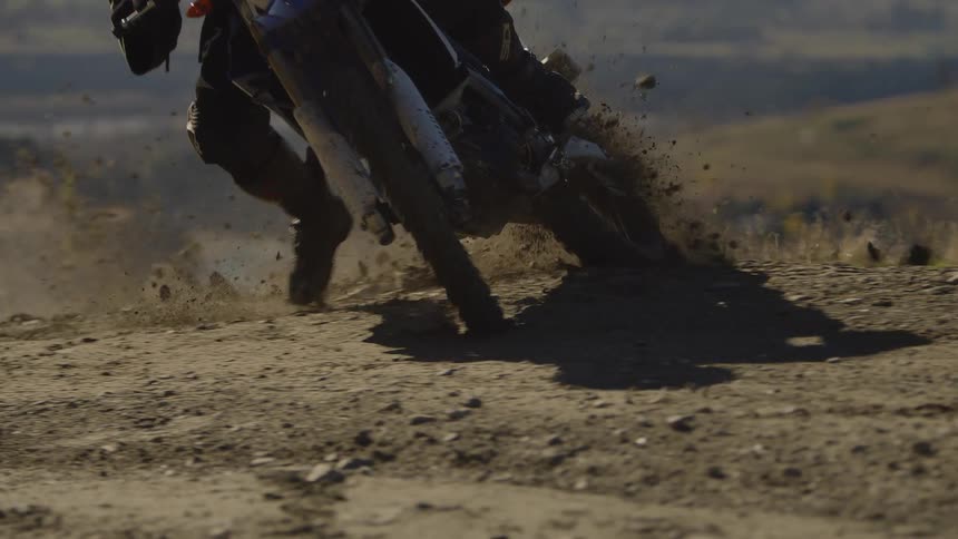 A person riding a dirt bike and skidding around a corner on a trail kicking up dirt