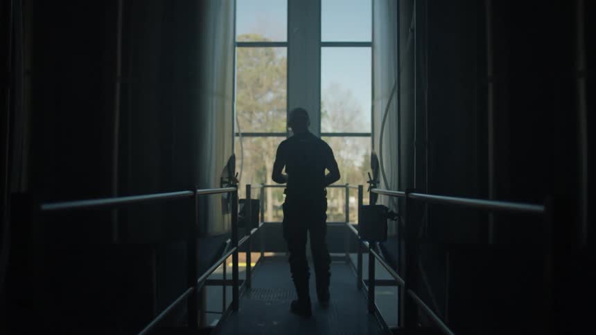Man walks down a hallway and kneels down to look at a metal fence