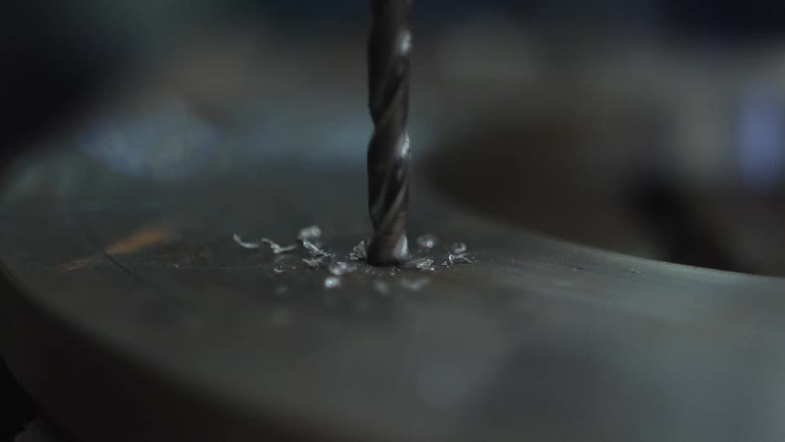 Metal shavings scatter across smooth metal surface and into air as drill bit drills into metal