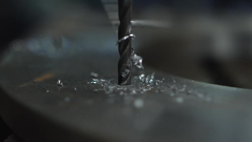 A drill in revolution creating a hole in a metal surface