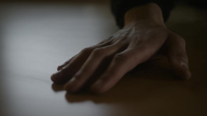 Close up of the hand of a person sliding over a wooden table on a dimly lit room