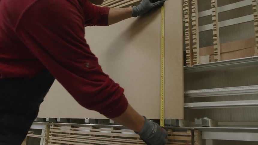 A person holds a tape measure up toa board in order to check its dimensions