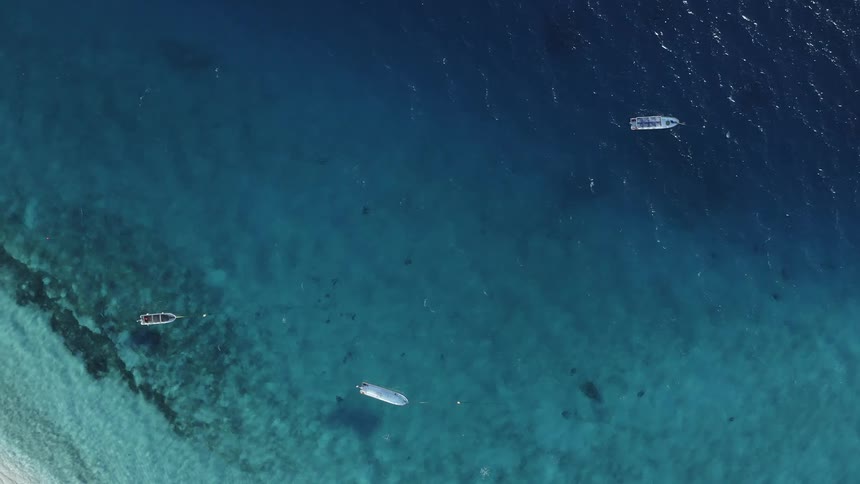 Boats float on water allowing glimpses of seafloor as waves retreat from beach