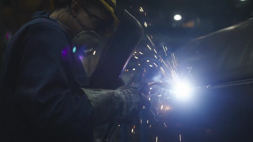 Close up of a welder working on a large piece of metal in a factory
