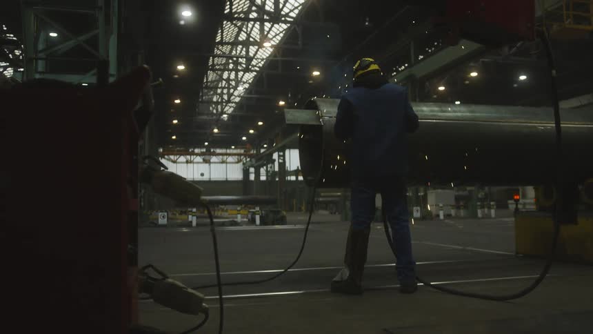 A man is standing in a garage with his back turned as he works and sparks fly into the air