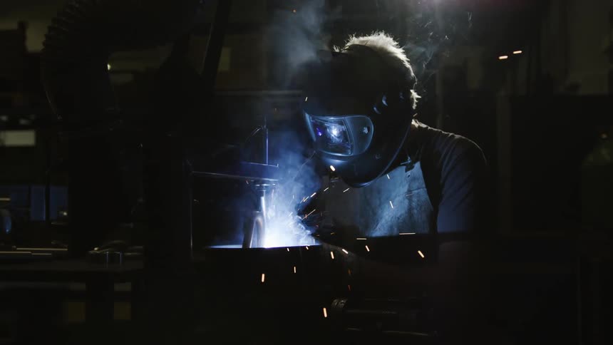 A man with a mask and apron is welding in a dark room