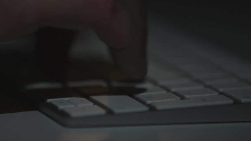 Close up of the hands of a man typing on the keyboard of a computer under flashing lights