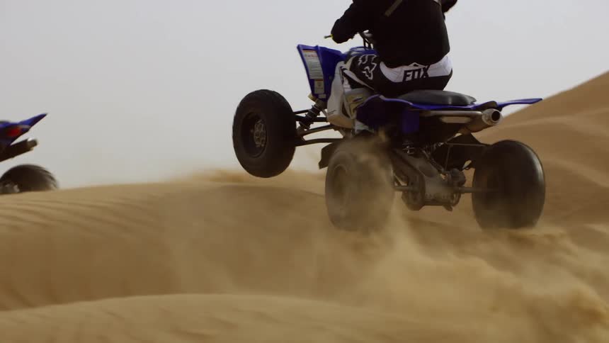 Two people drive quad bikes over the sand dunes in the desert at daytime