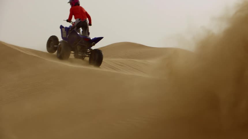 Two people riding four wheelers up and over sand dunes
