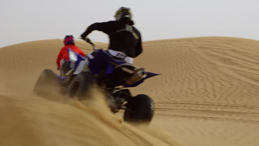 Two people are riding vehicles through a desert
